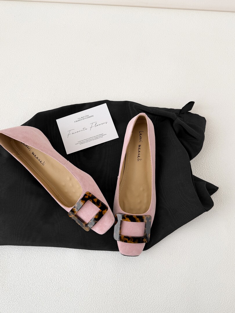 Pink women's flats with tortoiseshell buckle detail on a black fabric background
