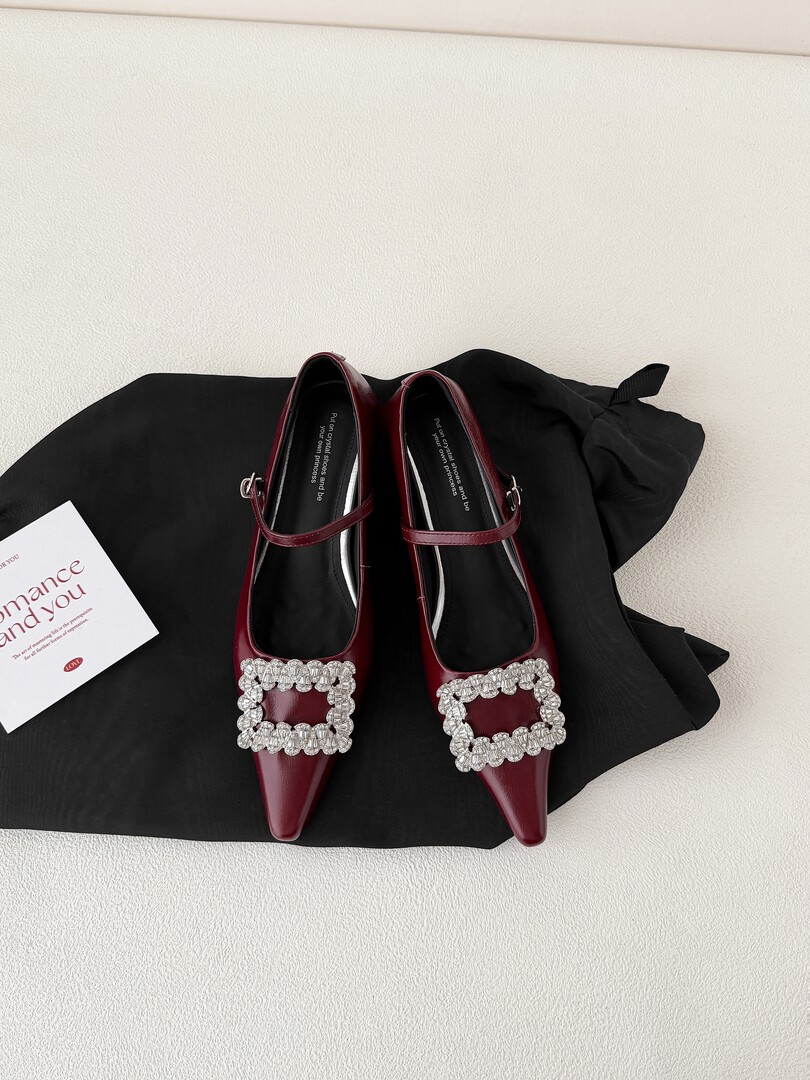 Burgundy pointed-toe embellished flats on a black fabric background
