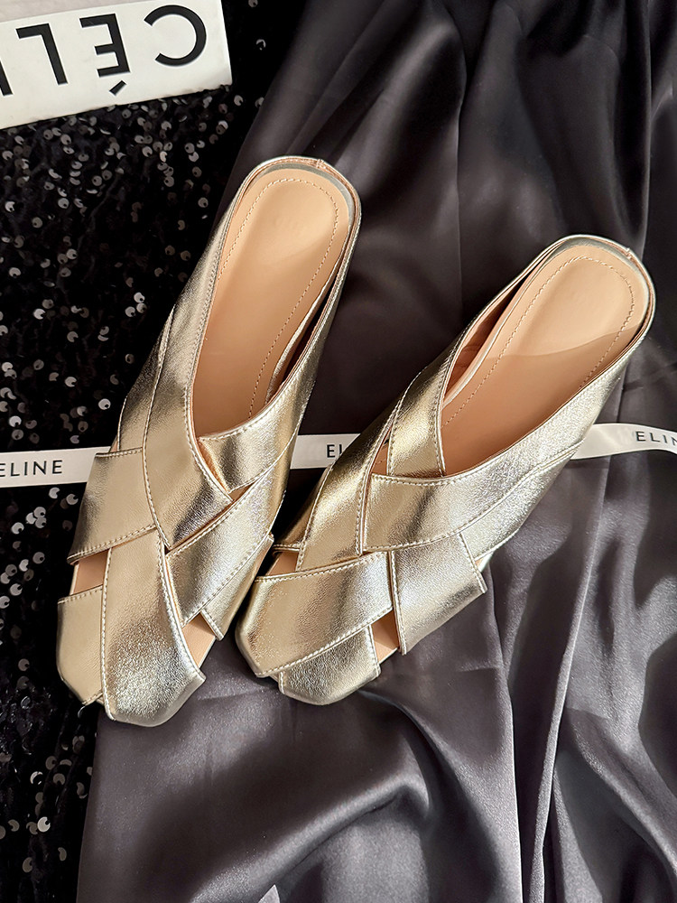 Metallic gold crisscross mule heels laid flat on dark fabric