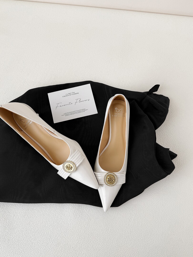 Pair of white pointed-toe flats with gold floral buckles on black fabric