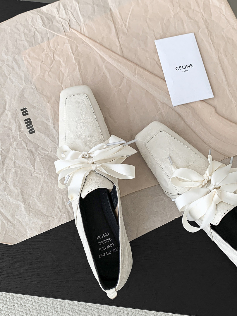 White pointed-toe flat shoes with ribbon bows displayed on packaging