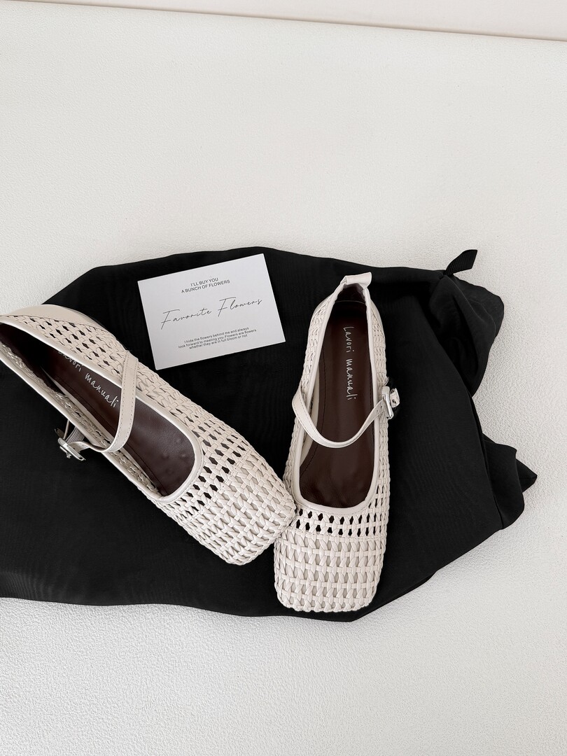 Pair of white woven flat shoes displayed on a black cloth background