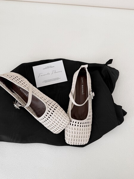 Pair of white woven flat shoes displayed on a black cloth background