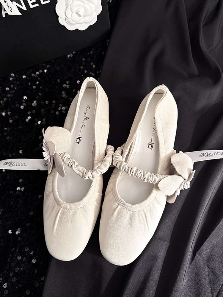 Cream ballet flats with ribbon ties and bow details on a dark fabric background