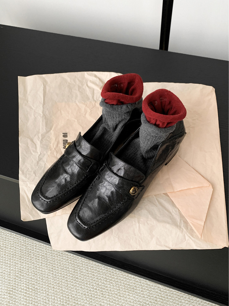 Black leather loafers with gray and red socks on tissue paper