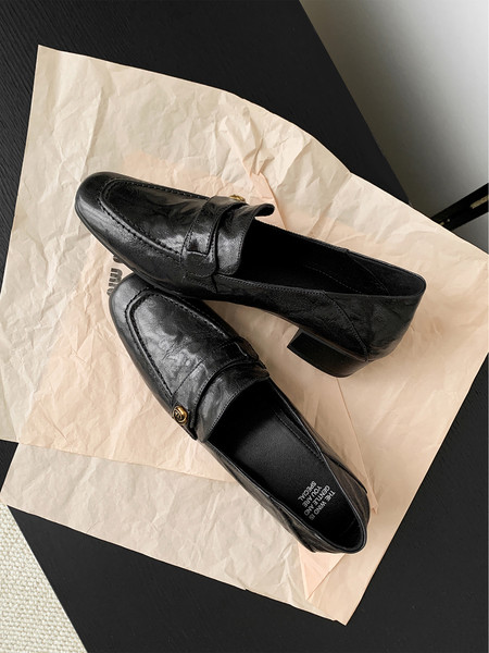 Pair of black leather loafers displayed on paper packaging