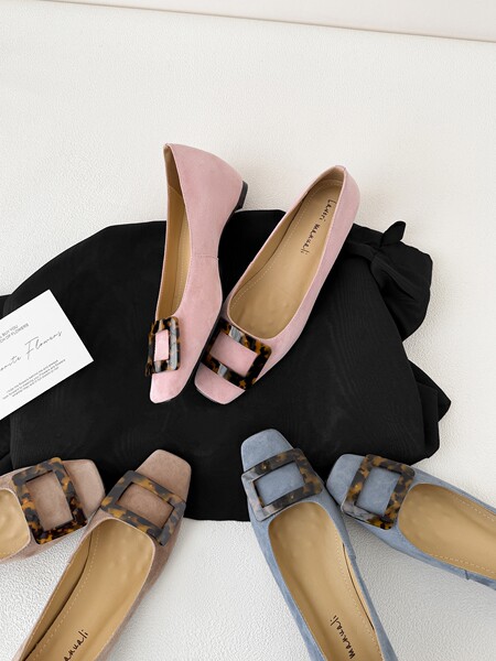 Pastel pointed-toe flats with tortoiseshell buckle detail displayed on a background