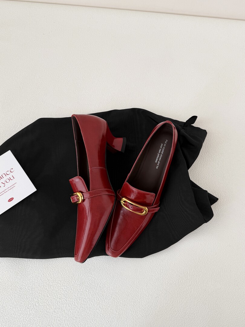 Pair of burgundy pointed-toe loafers with gold buckle on a black fabric background