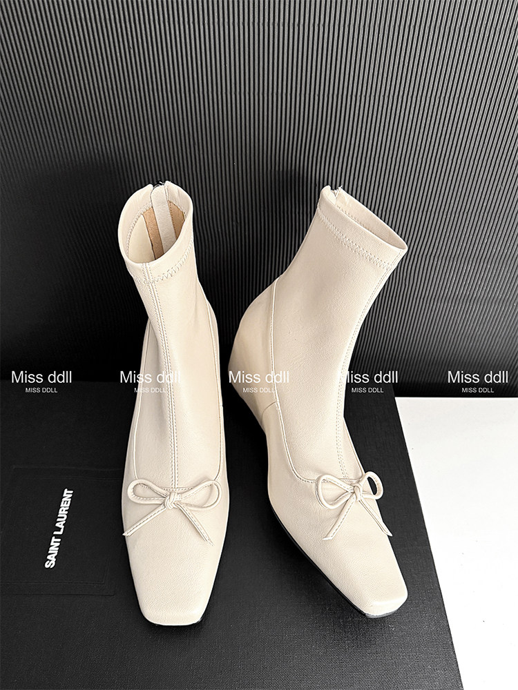 Cream ankle boots with pointed toes and bow detail on a black background