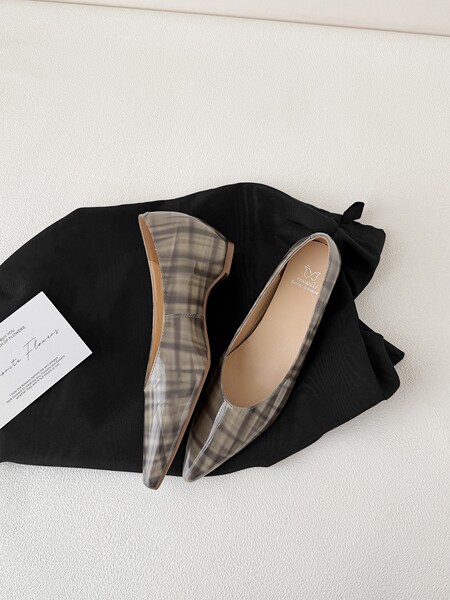 Pair of plaid pointed-toe flat shoes on a black fabric background