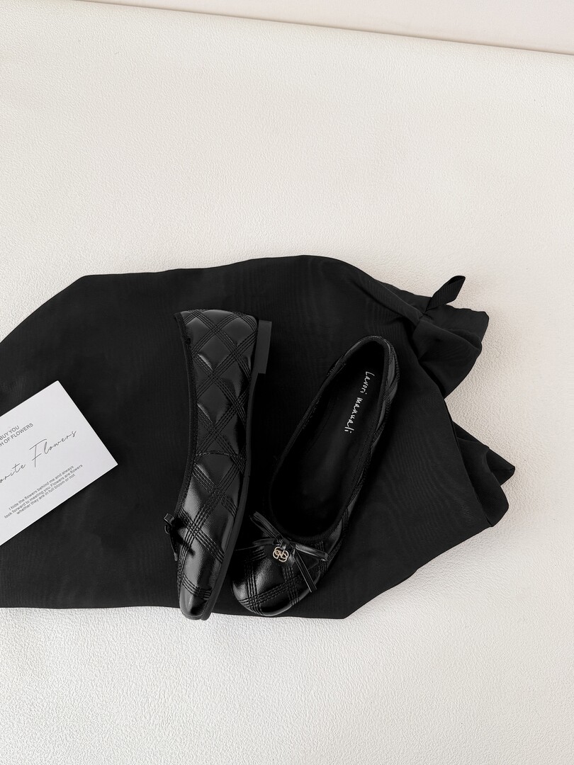 Black quilted flats shoes displayed on a black fabric background
