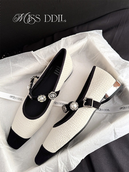Pair of cream and black textured embellished flats displayed on packaging