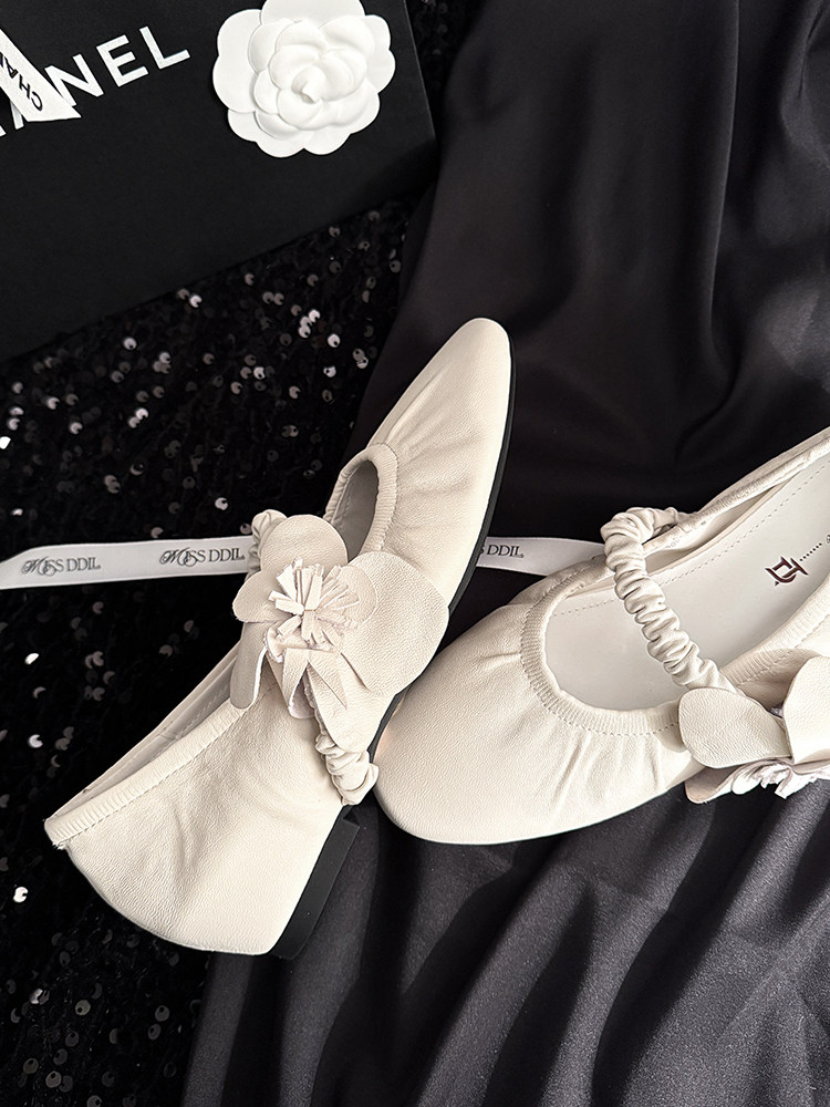 Cream pointed-toe flats with floral embellishment on a dark fabric background