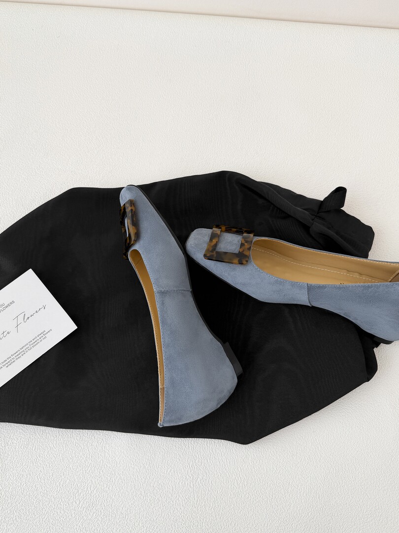 Pair of light blue pointed flats with tortoiseshell buckle detail on a black fabric background