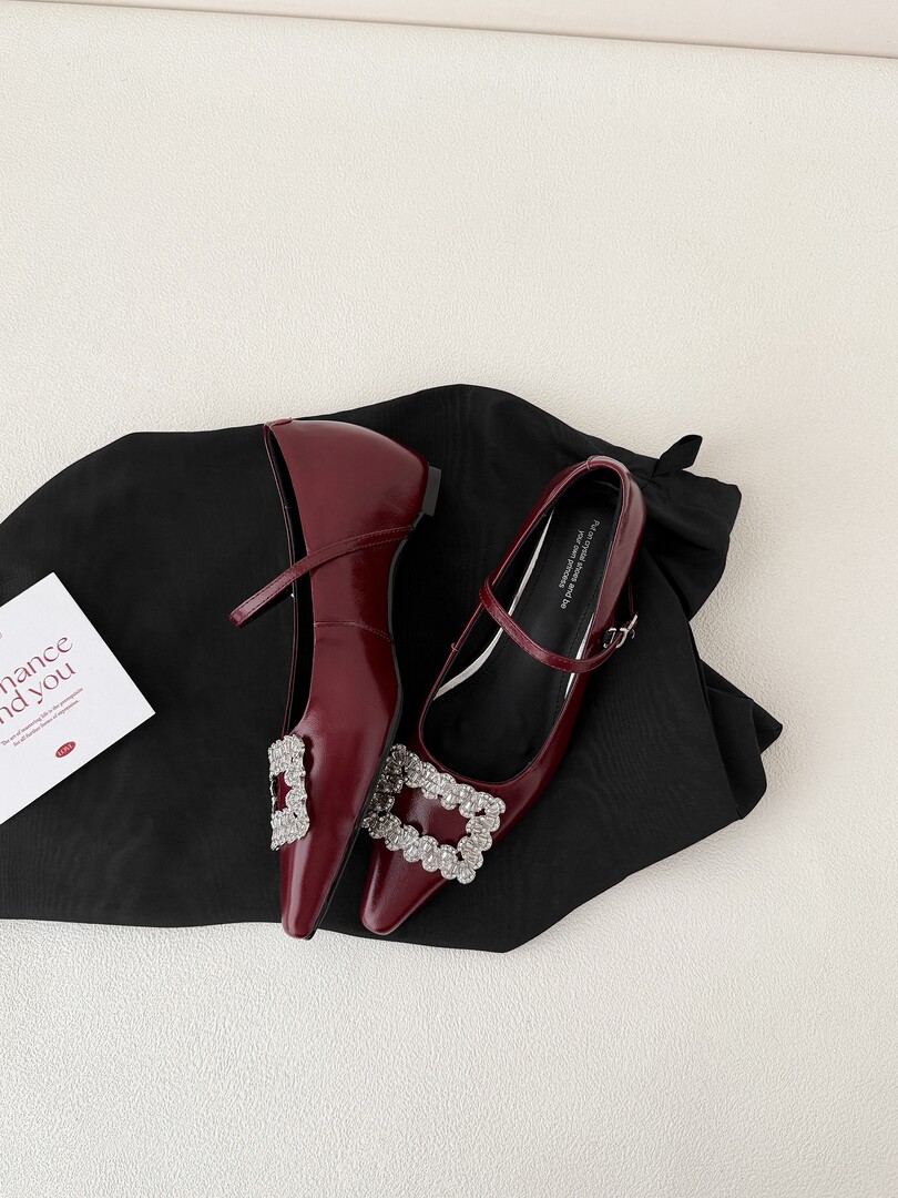 Burgundy pointed-toe embellished Mary Jane flats on a black cloth background