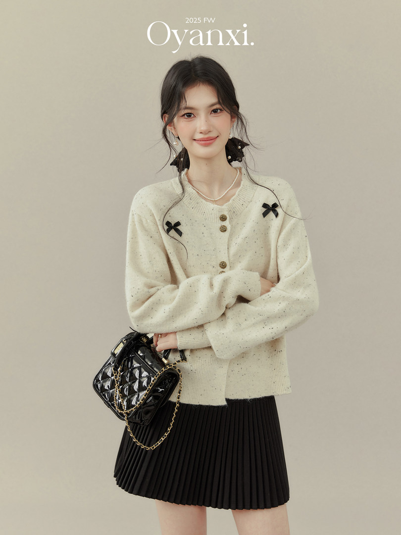 Model wearing a cream cardigan with black pleated skirt and black handbag