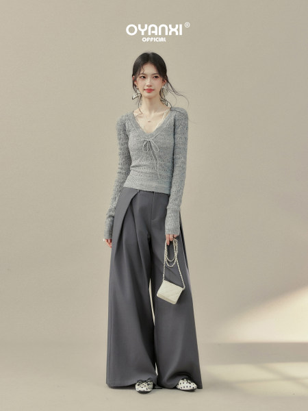 Model wearing a gray knit top and wide-leg charcoal pants with a small chain handbag