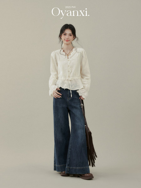 Model wearing a white ruffled blouse with wide-leg dark denim jeans and a brown fringe shoulder bag