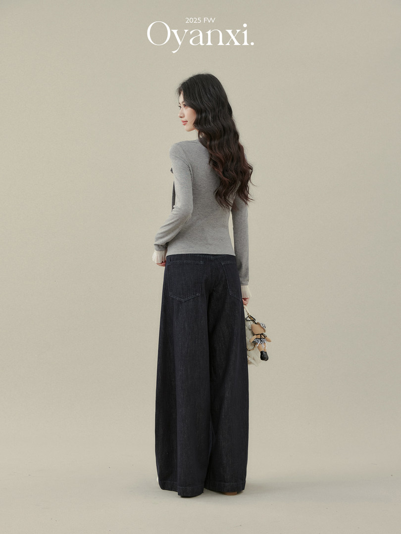 Model wearing a gray fitted top and dark wide-leg jeans on a plain background