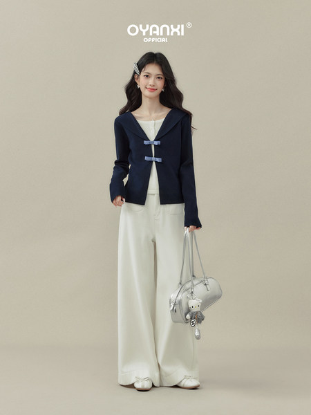 Woman modeling a navy sailor-style top with white wide-leg pants and a silver handbag