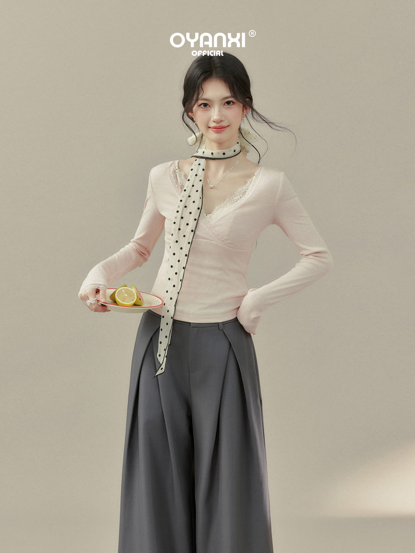 Model wearing a light pink lace-trim long-sleeve top with a polka dot scarf and gray wide-leg trousers