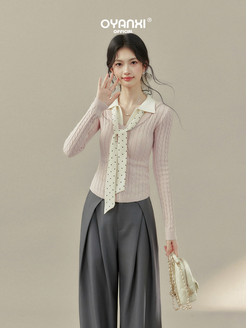 Model wearing a pink knit sweater with scarf detail, gray wide-leg pants, and a small quilted handbag