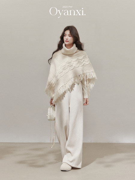 Model wearing a cream knit turtleneck poncho with wide-leg pants and a small handbag