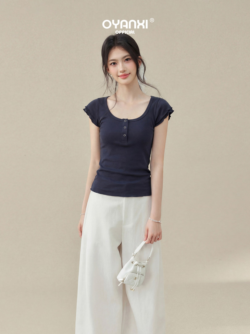 Model wearing a navy short-sleeve button-front top with white wide-leg pants and a small white handbag