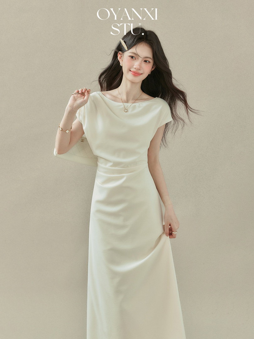 Woman wearing a cream satin dress with a white handbag