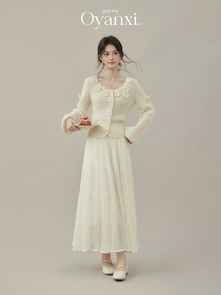 Model wearing a cream knit floral cardigan with a flowing white skirt
