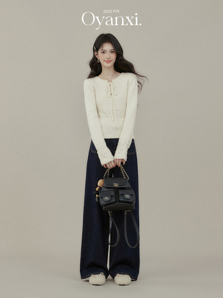 Model wearing a cream knit sweater with dark wide-leg jeans and a black backpack