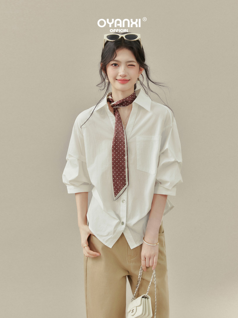 Model wearing a white button-up shirt with a brown neck scarf and beige trousers