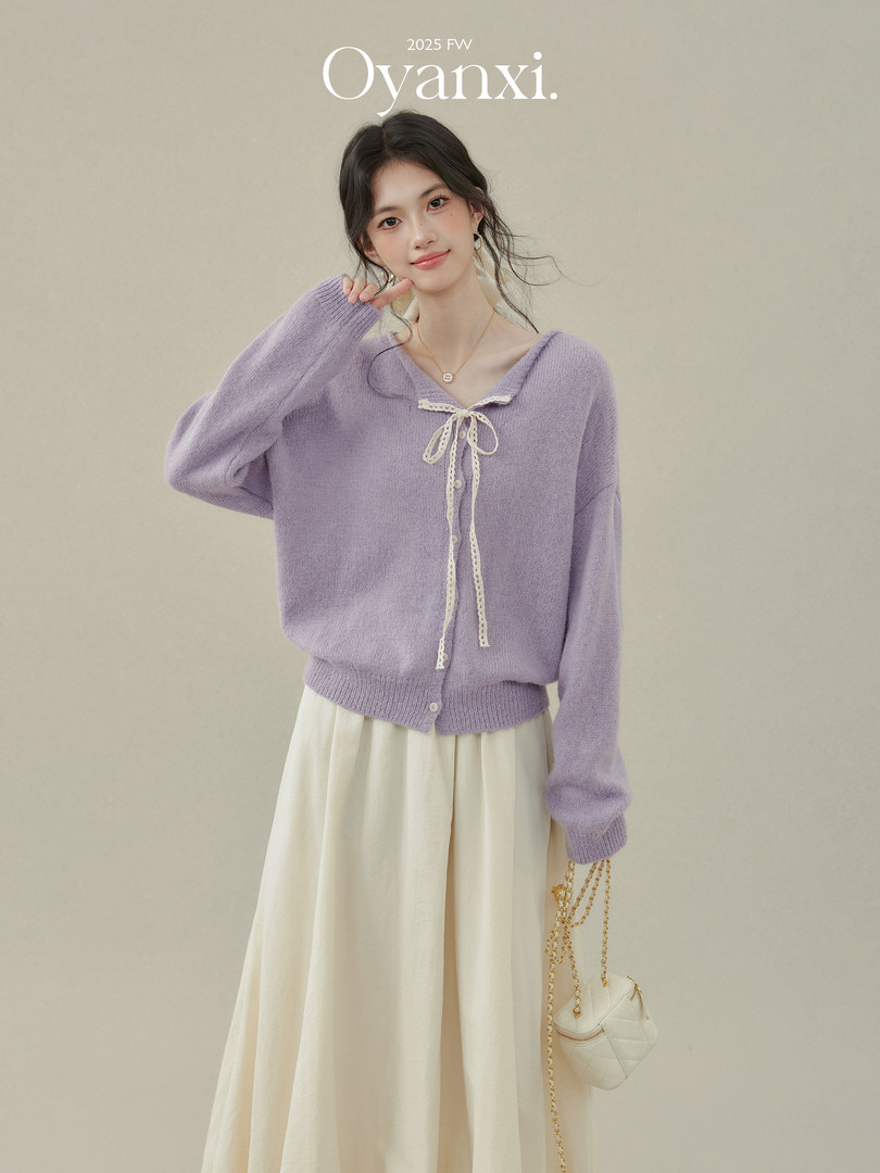 Model wearing a lavender knit cardigan with cream skirt and small chain bag