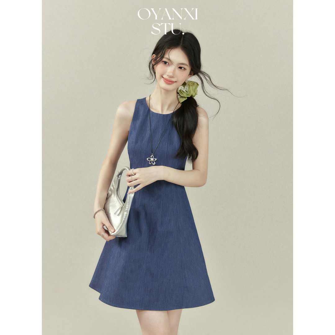 Model wearing a sleeveless blue A-line dress with a silver handbag