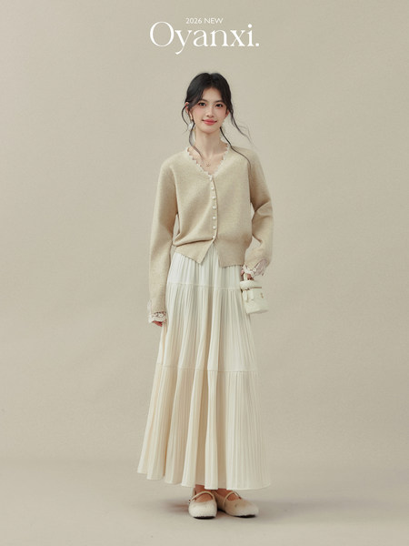 Model wearing a beige cardigan with a cream pleated long skirt and matching flats