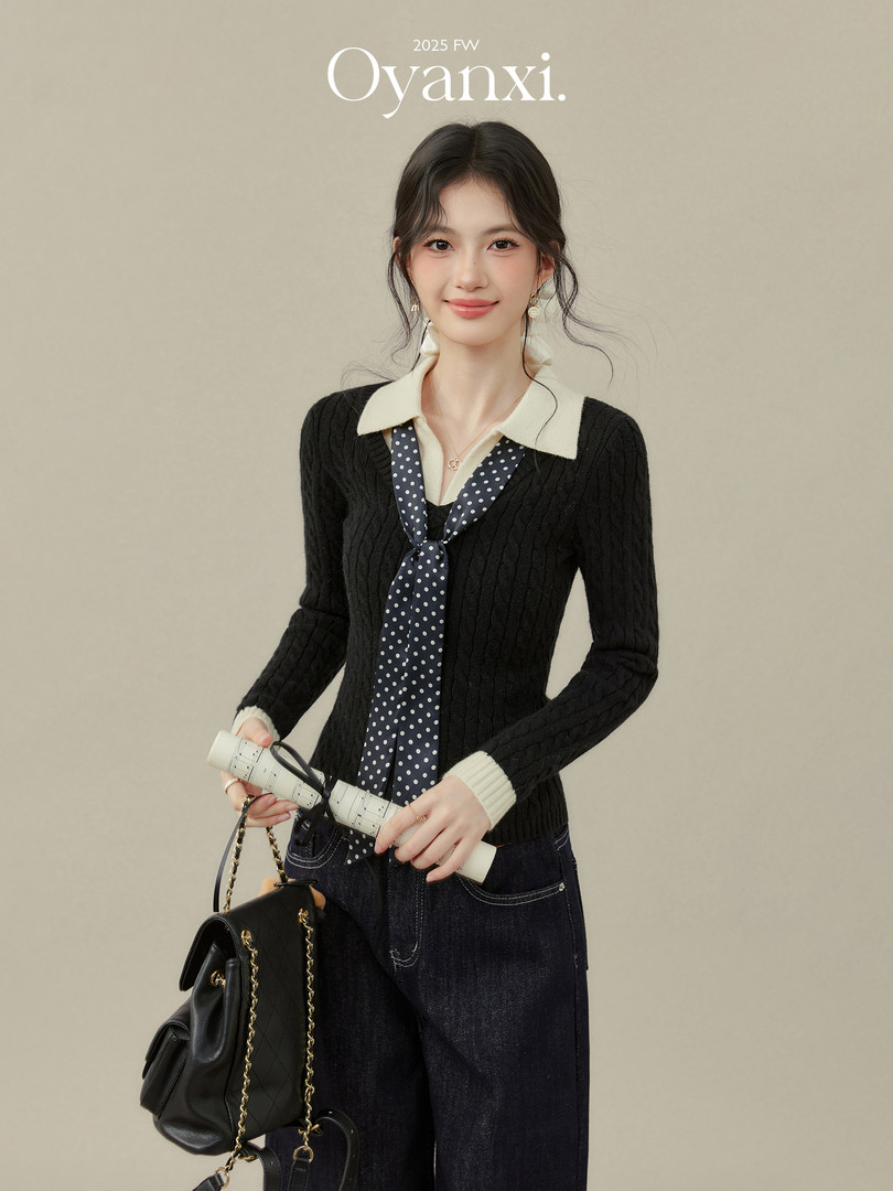 Model wearing a black knit top with a white collar and polka dot tie, holding a black handbag