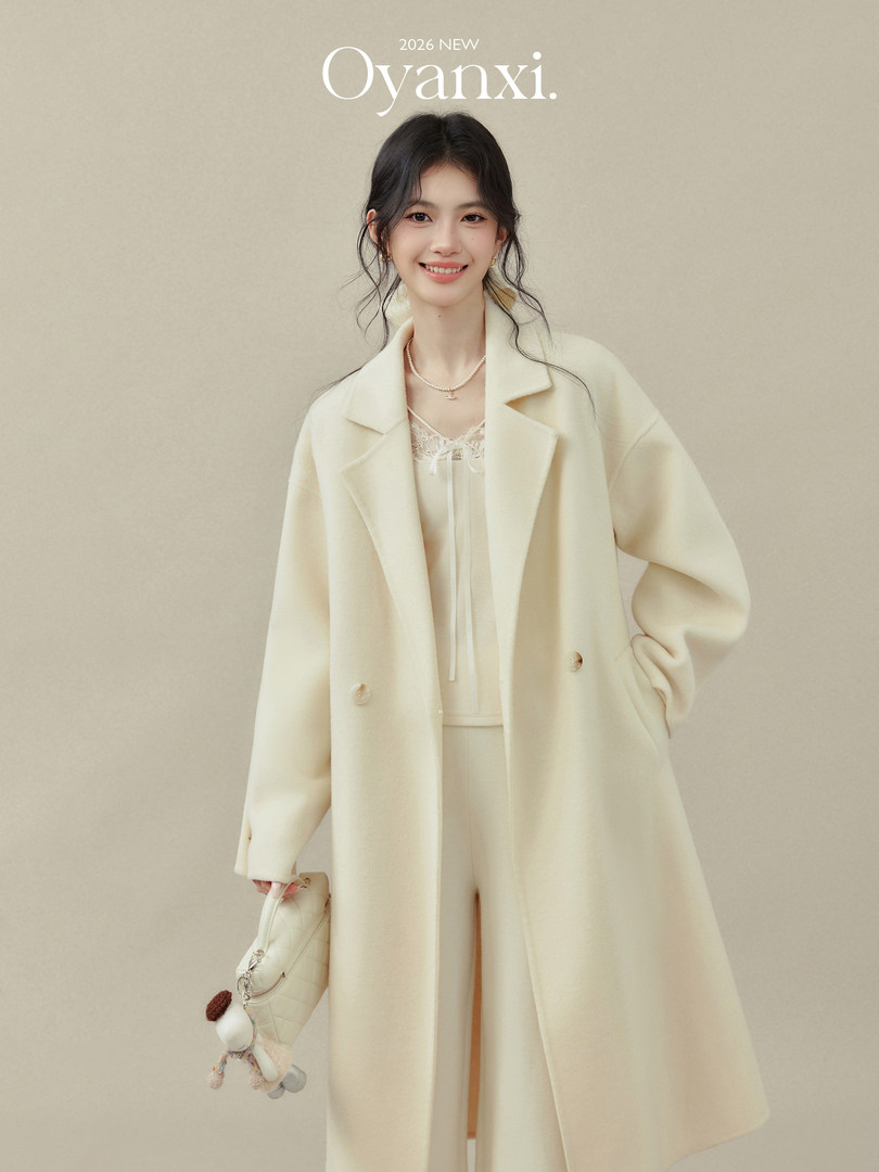 Model wearing a cream long coat with matching outfit and handbag