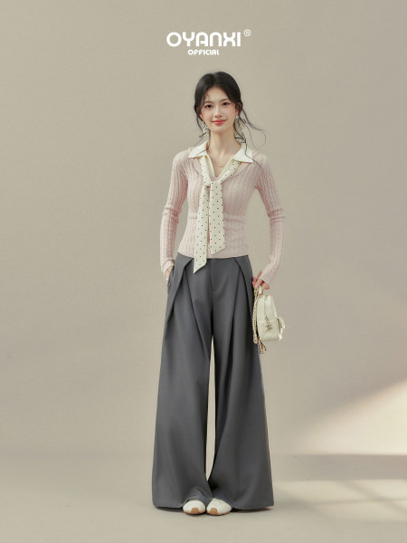 Fashion model wearing a pink knit top with scarf detail and wide-leg gray pants