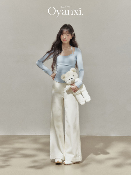 Woman modeling a light blue long-sleeve top with white wide-leg pants and holding a teddy bear
