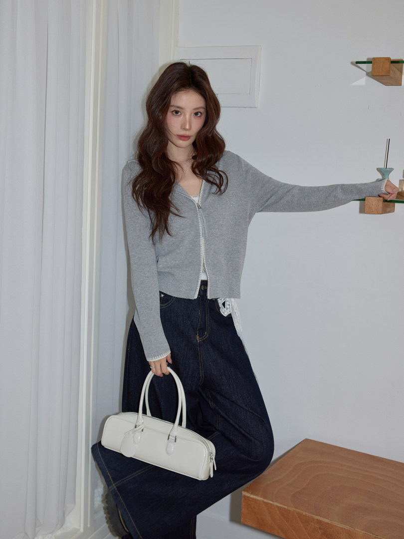 Model wearing a gray zip-front cardigan, dark jeans, and holding a white handbag