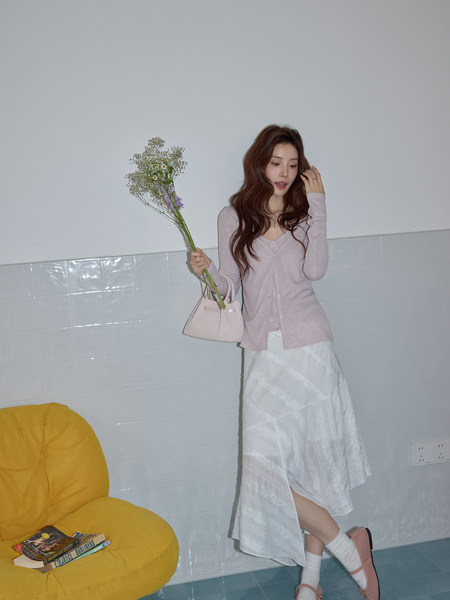 Woman modeling a light pink cardigan and white skirt with a small handbag