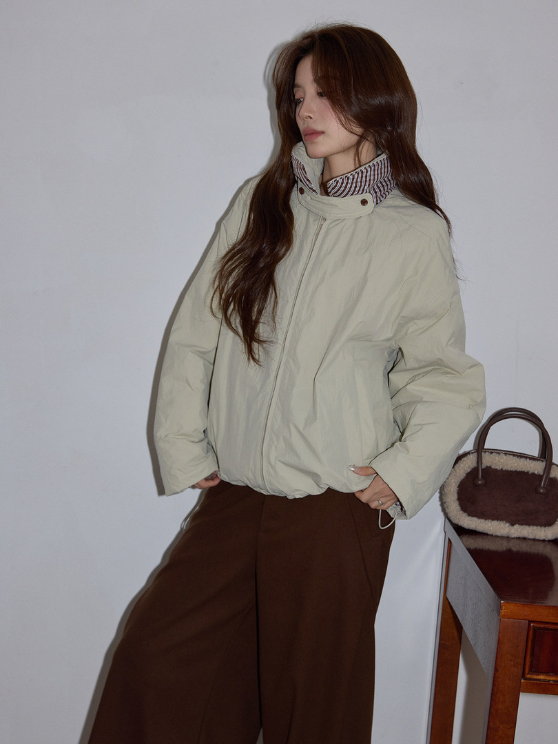 Model wearing a light beige zip-up jacket with a high collar and brown skirt