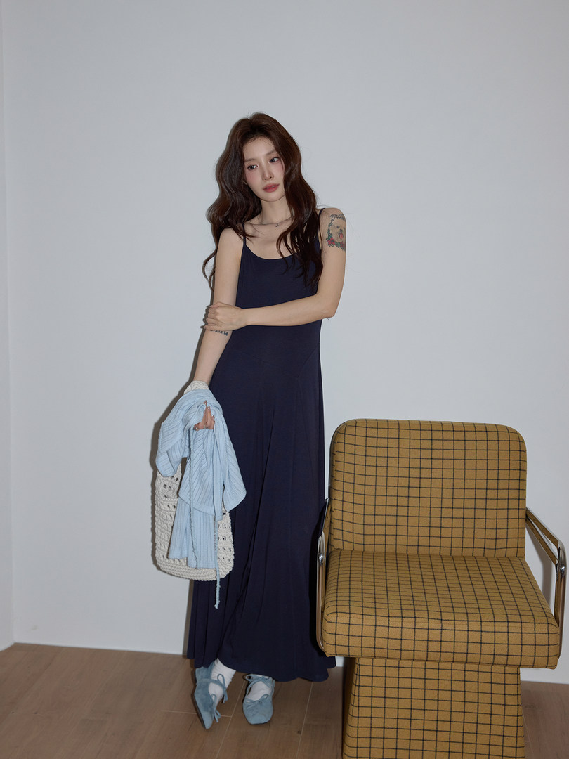 Model wearing a navy sleeveless maxi dress with light blue flats and holding a knit bag and sweater