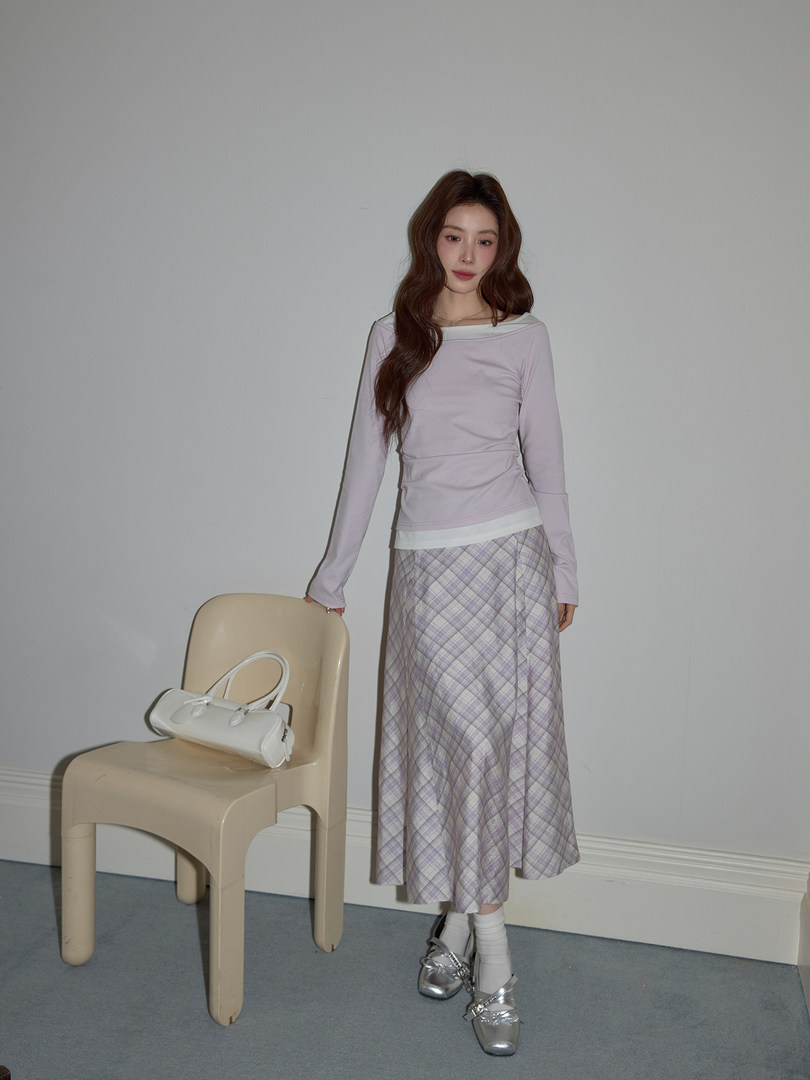 Model wearing a pastel long-sleeve top with a plaid midi skirt, silver shoes, and a white handbag