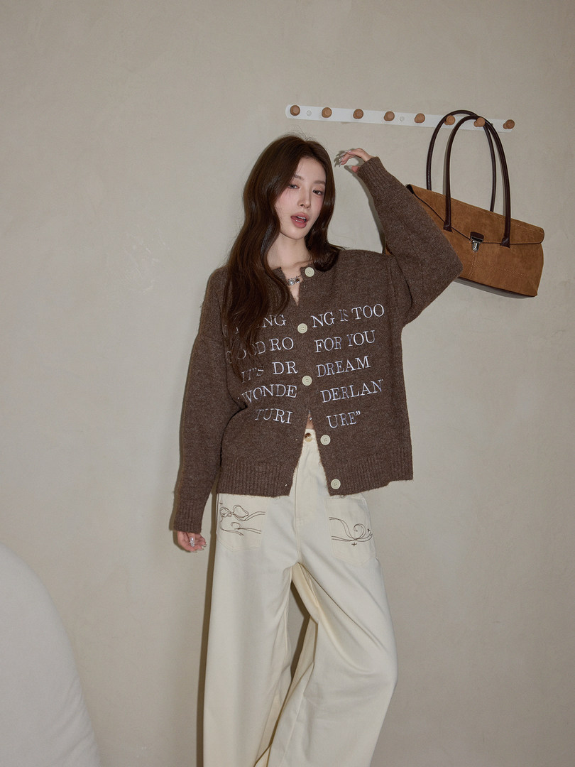 Model wearing a brown knit cardigan and cream wide-leg pants with a tan handbag