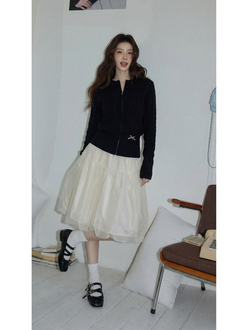 Model wearing a black zip-front top with a cream tiered skirt and black strap shoes