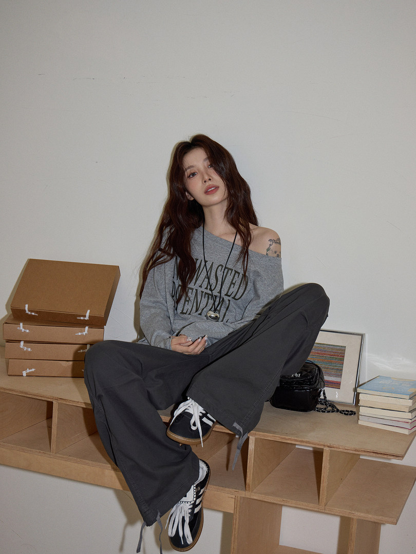 Model wearing an off-shoulder graphic long-sleeve top with black wide-leg pants and sneakers