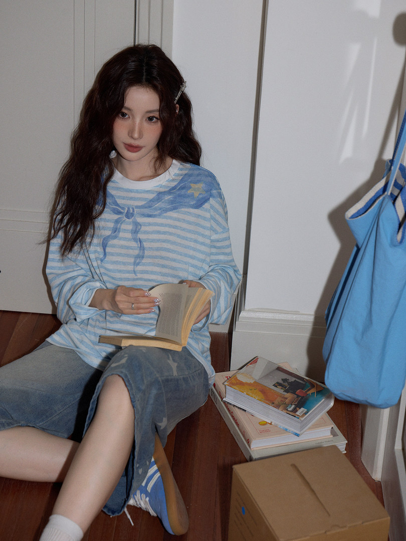 Woman wearing a light blue striped long-sleeve top and denim skirt while sitting on the floor