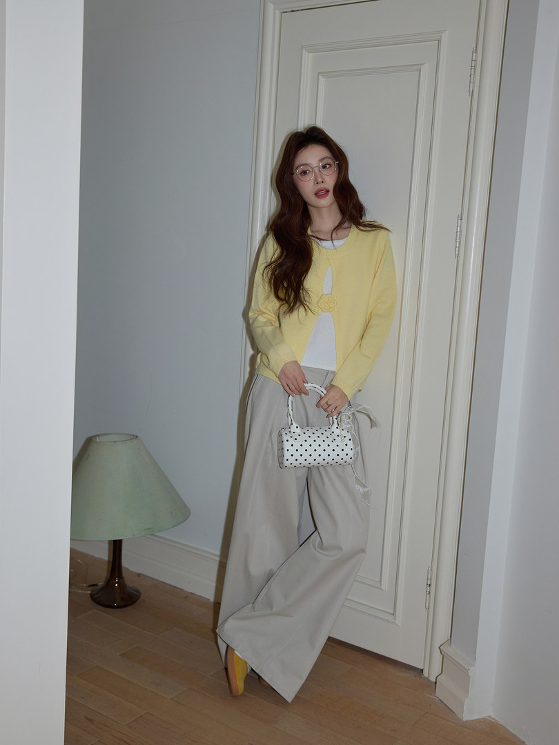 Model wearing a yellow cardigan with wide-leg light gray pants and a white polka dot handbag