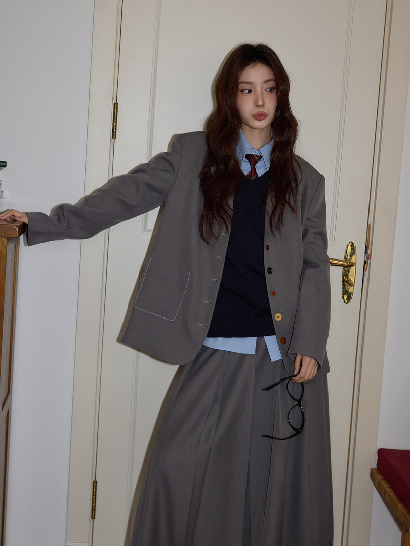 Model wearing a gray blazer and matching pleated skirt with a blue shirt and tie